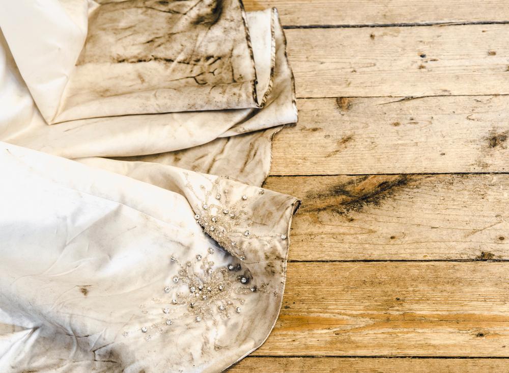 Detail view of a beautiful white wedding dress train after the outdoor wedding on a rainy day on a wooden board background. Needing a dry-cleaning concept.