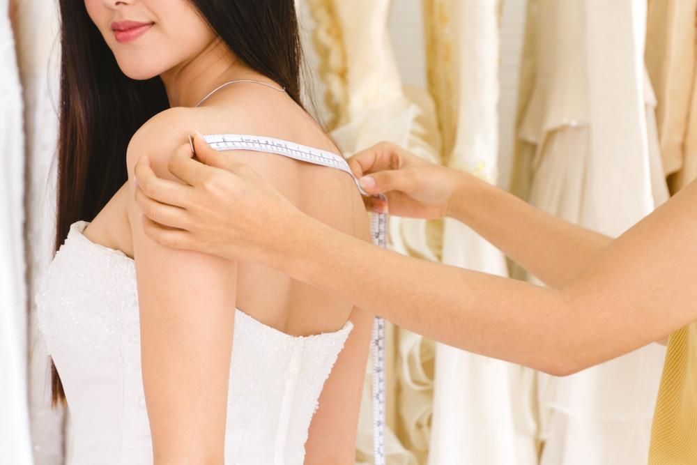 Female dressmaker measuring woman's back for a wedding dress alteration