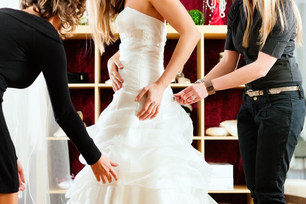 Bride at the clothes shop for wedding dresses; she is choosing a dress and the designer are assisting her.