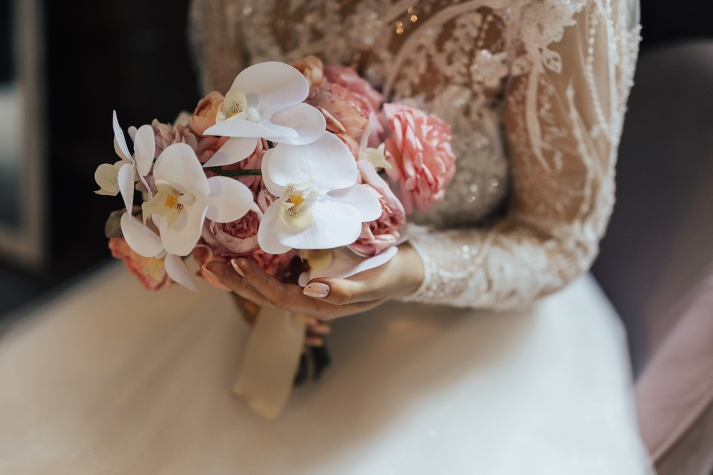 Wedding bouquet with white and rose fresh flowers in the hands of the bride. Cropped shot.